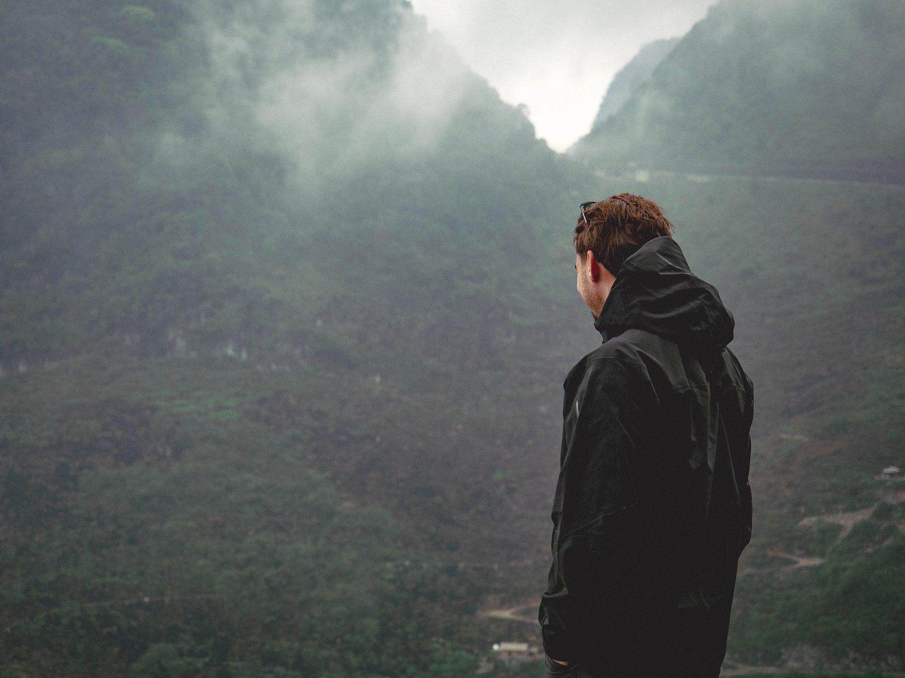 A man in a dark jacket looking out into thick fog between mountain slopes