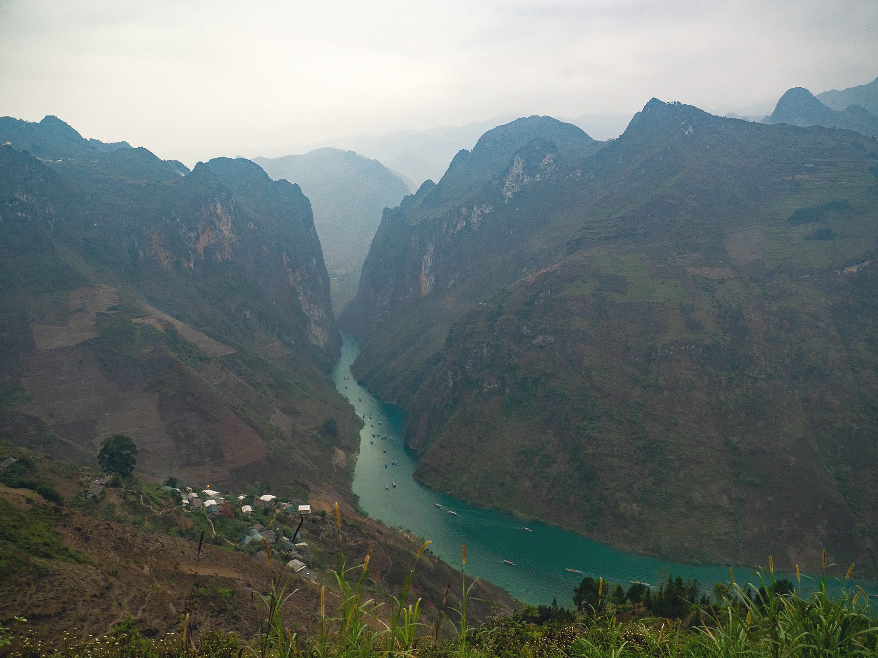 Turquoise river winding through a deep mountain canyon in Ha Giang under a hazy sky